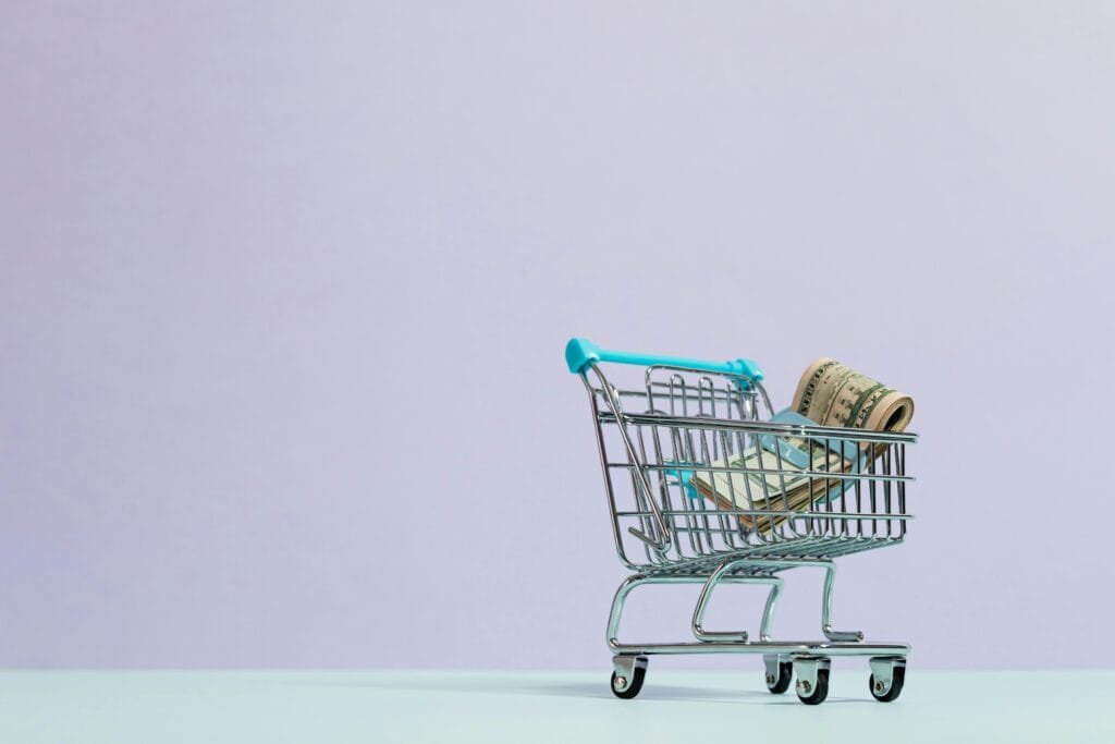 A close-up of a mini shopping cart with rolled cash on a pastel background. Ideal for finance and ecommerce themes.